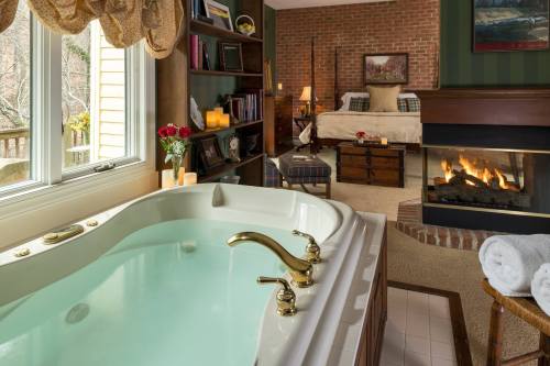 Cozy bedroom with a fireplace, a jetted tub, and bookshelves, featuring candles and roses for a relaxing atmosphere.