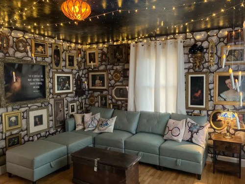 Cozy living room with a blue sectional sofa, vintage decor, framed pictures on the walls, and warm string lights.