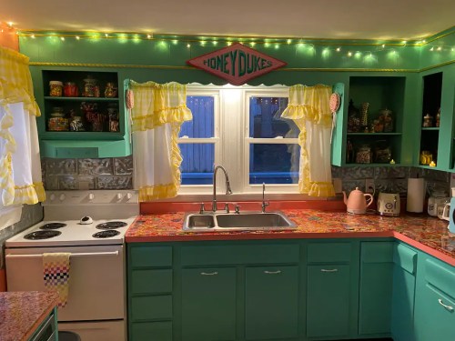 Brightly colored kitchen with teal cabinets, pink countertops, and fairy lights, featuring a vintage "Honeydukes" sign.
