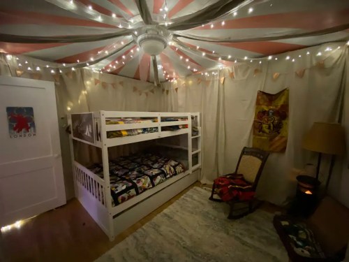 Cozy bedroom with a bunk bed, string lights, and a vintage chair, featuring soft colors and a whimsical ceiling design.