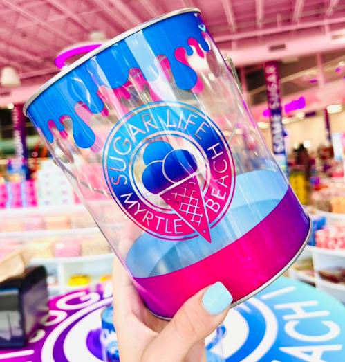 A colorful ice cream-themed container with "Sugar Life Myrtle Beach" logo, held against a vibrant store background.