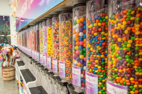 A colorful display of candy-filled dispensers lined up on a shelf, showcasing various types of sweets.
