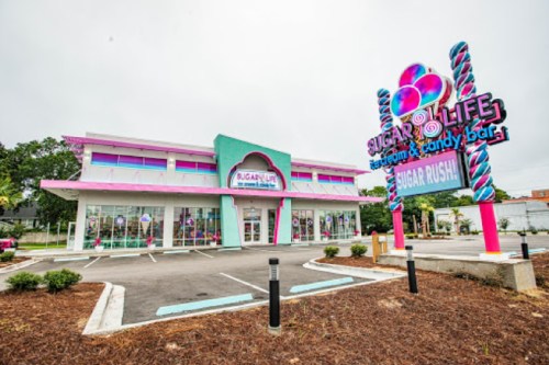 Colorful storefront of "Sugar Life" featuring a candy bar, with a vibrant sign and pink accents.