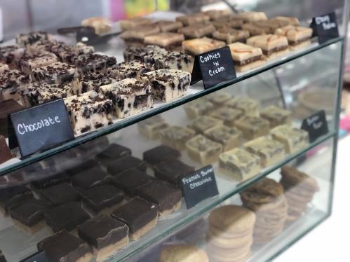 A display case filled with various types of fudge and cookies, labeled with flavors like chocolate and cookies & cream.
