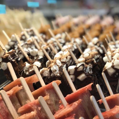 Colorful ice pops on sticks, featuring various flavors and toppings, displayed in a row.