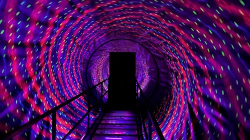 A colorful, swirling tunnel with vibrant lights leading to a dark doorway at the end.