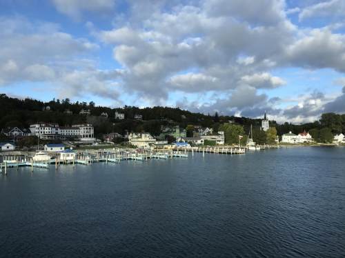 A scenic waterfront view of a small town with boats, houses, and a church under a partly cloudy sky.