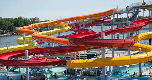 Colorful water slides twist and turn above a pool, with people enjoying the water below on a sunny day.