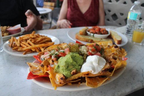 A plate of nachos topped with guacamole, sour cream, and salsa, accompanied by fries and a side of fresh salsa.