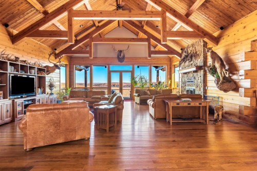 Spacious rustic living room with wooden beams, large windows, and cozy furniture, featuring a stone fireplace and decor.