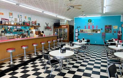 A retro diner with checkered floors, red and silver stools, and a colorful counter, evoking a nostalgic atmosphere.