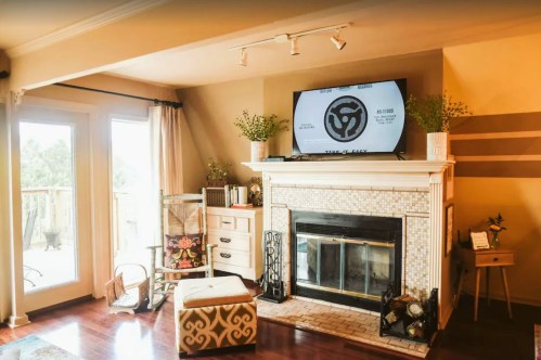 Cozy living room with a fireplace, TV on the mantel, and stylish decor, featuring a mix of modern and vintage elements.