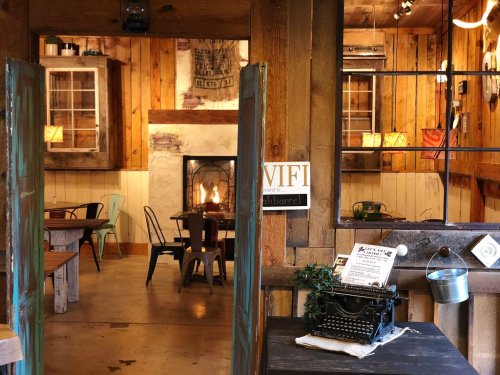 Cozy rustic interior of a café with wooden decor, a fireplace, and tables set for dining.