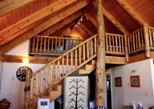 A cozy wooden interior featuring a staircase with log railings and a high ceiling, adorned with rustic decor.