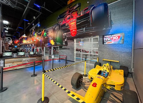 A vibrant indoor racing venue featuring a yellow race car, colorful wall murals, and a lunch special sign.