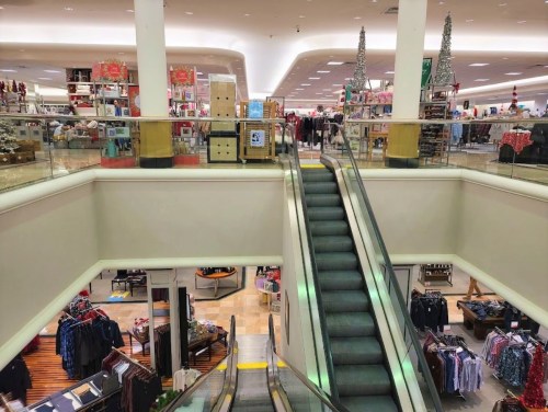 A view of a multi-level store with escalators, shelves of merchandise, and holiday decorations in the background.