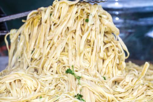 A close-up of freshly cooked fettuccine pasta, lightly coated in oil and garnished with parsley.