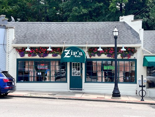 Exterior of Zip's Cafe, featuring colorful flower boxes, neon signs, and a welcoming entrance under a green awning.