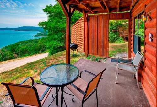 A cozy porch with a table and chairs overlooking a scenic lake and lush greenery.