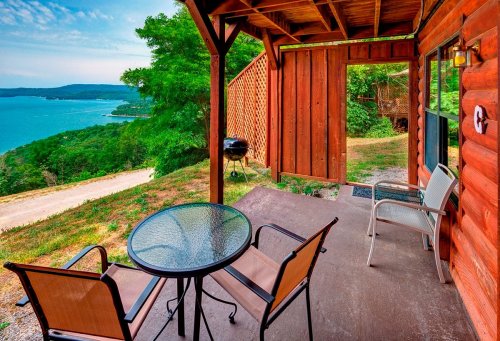 A cozy porch with a table and chairs overlooking a scenic lake and lush greenery.