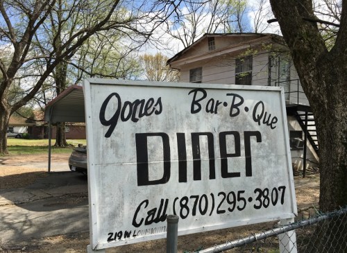 Sign for "Jones Bar-B-Que Diner" with a phone number, set in a rural area with trees and a house in the background.