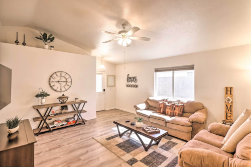 Cozy living room with a ceiling fan, beige sofas, a coffee table, and decorative wall art in a bright, inviting space.