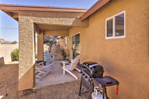 A patio area with two white chairs, a grill, and a view of a beige house and garden.