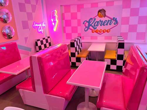 Colorful diner interior featuring pink booths, checkered seating, and neon signs. Bright and playful atmosphere.