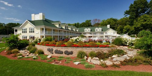 A scenic view of a yellow resort building surrounded by colorful flowers and greenery under a clear blue sky.