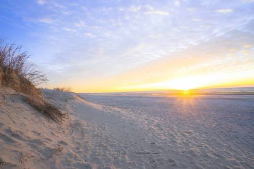 A serene beach at sunset, with soft sand dunes and a colorful sky reflecting the fading light.