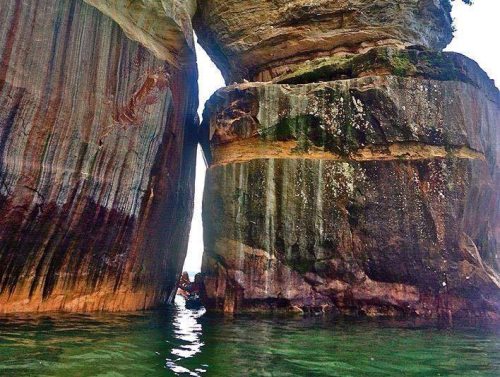 Two towering rock formations with a narrow gap between them, partially submerged in clear water.