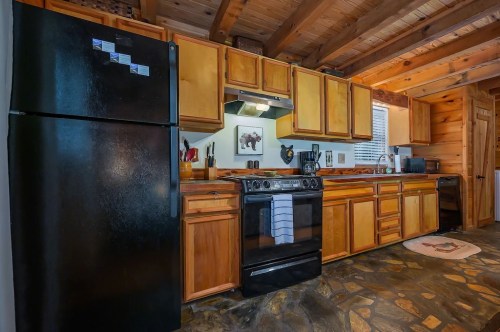 Cozy kitchen with wooden cabinets, black appliances, and stone floor, featuring a rustic, cabin-like atmosphere.