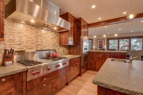 Modern kitchen with stainless steel appliances, wooden cabinets, and a stone backsplash, featuring a spacious layout.