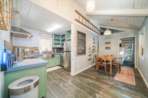 Cozy kitchen and dining area with wooden floors, green cabinets, and a chalkboard wall in a bright, inviting space.