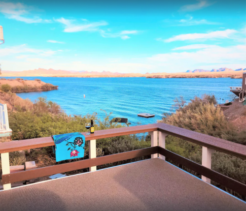 A scenic view of a lake with mountains in the background, featuring a deck with a towel and a bottle.
