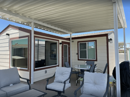 A cozy outdoor patio with seating, a table, and a small house under a shaded awning.