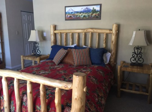 Cozy bedroom featuring a log bed, colorful bedding, and rustic lamps on wooden nightstands. Mountain artwork on the wall.