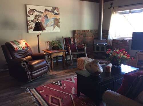 Cozy living room with leather chairs, a wooden table, a fireplace, and colorful decor, featuring a rug and plants.