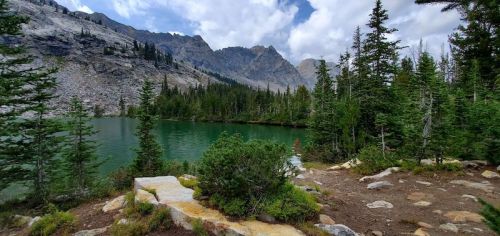 A serene lake surrounded by lush trees and mountains under a partly cloudy sky.