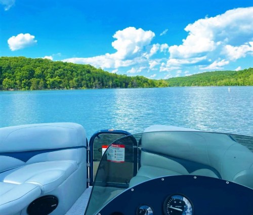 A scenic view from a boat, showcasing calm water, lush green hills, and a bright blue sky with fluffy clouds.
