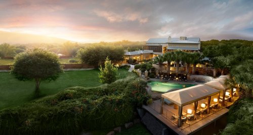 A scenic view of a luxurious resort at sunset, featuring a pool, lush greenery, and elegant outdoor seating.