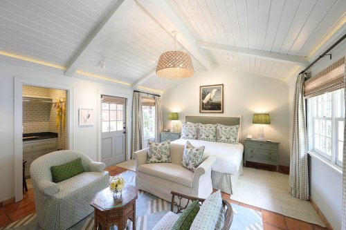 Cozy bedroom with a bed, floral decor, and a sitting area, featuring light walls and a bright, airy atmosphere.