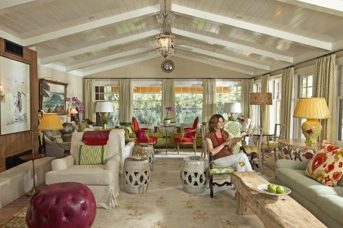 A cozy living room with a woman reading, featuring colorful furniture, large windows, and a warm, inviting atmosphere.