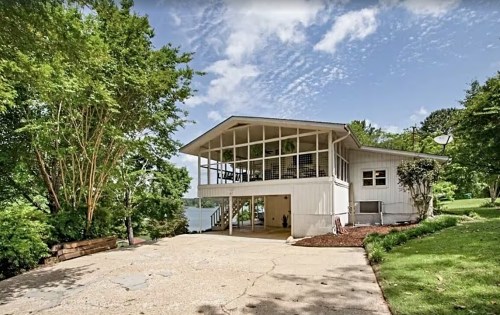 A modern two-story house with large windows, surrounded by greenery and a clear blue sky.