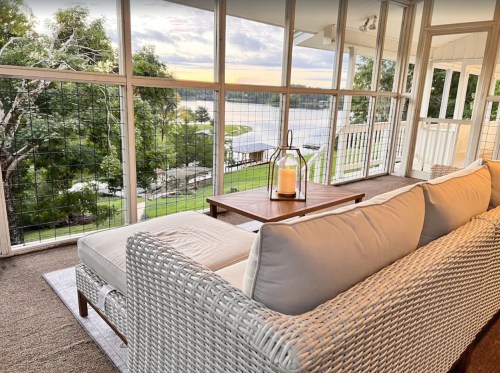 Cozy seating area with a view of a lake at sunset, featuring a lantern on a wooden table and large windows.
