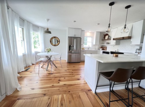 Bright kitchen with wooden floors, white cabinets, a round dining table, and modern lighting fixtures.
