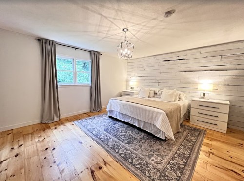 Bright bedroom with a wooden floor, white walls, a large bed, and a decorative rug, featuring natural light from a window.