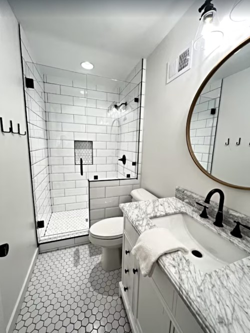 Modern bathroom featuring a walk-in shower, marble countertop, round mirror, and hexagonal tile flooring.