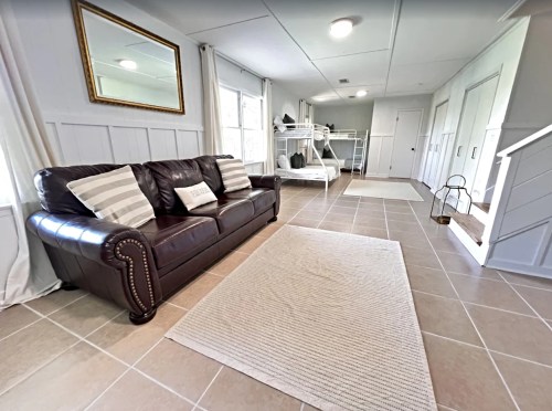 Cozy interior with a brown leather sofa, striped pillows, a rug, and a bunk bed in a well-lit room.
