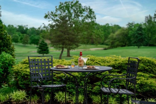 A table set for two with plates and a bottle of wine, surrounded by lush greenery and a scenic view.